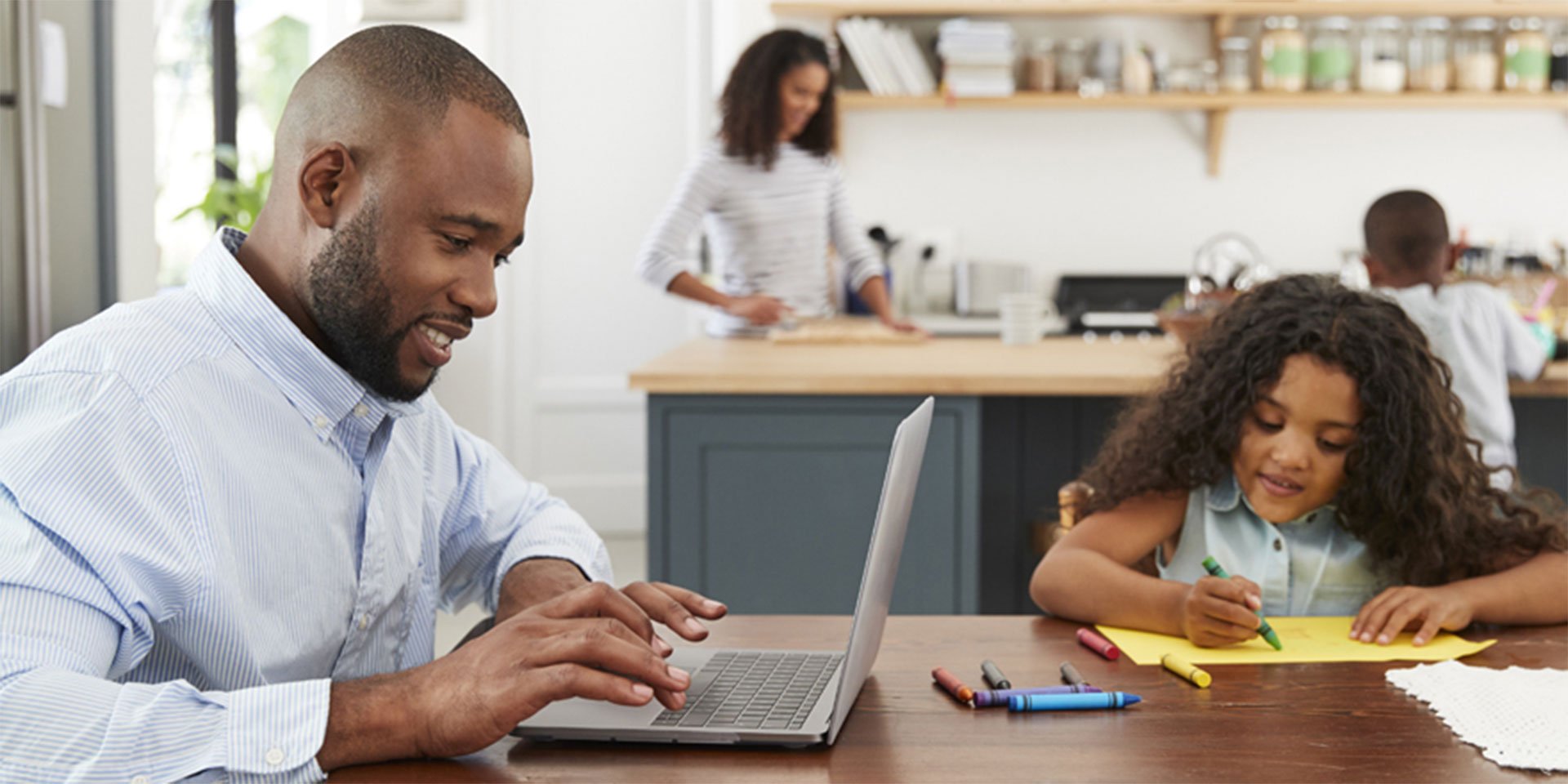 A family in the kitchen with the dad paying his loan payment on his laptop